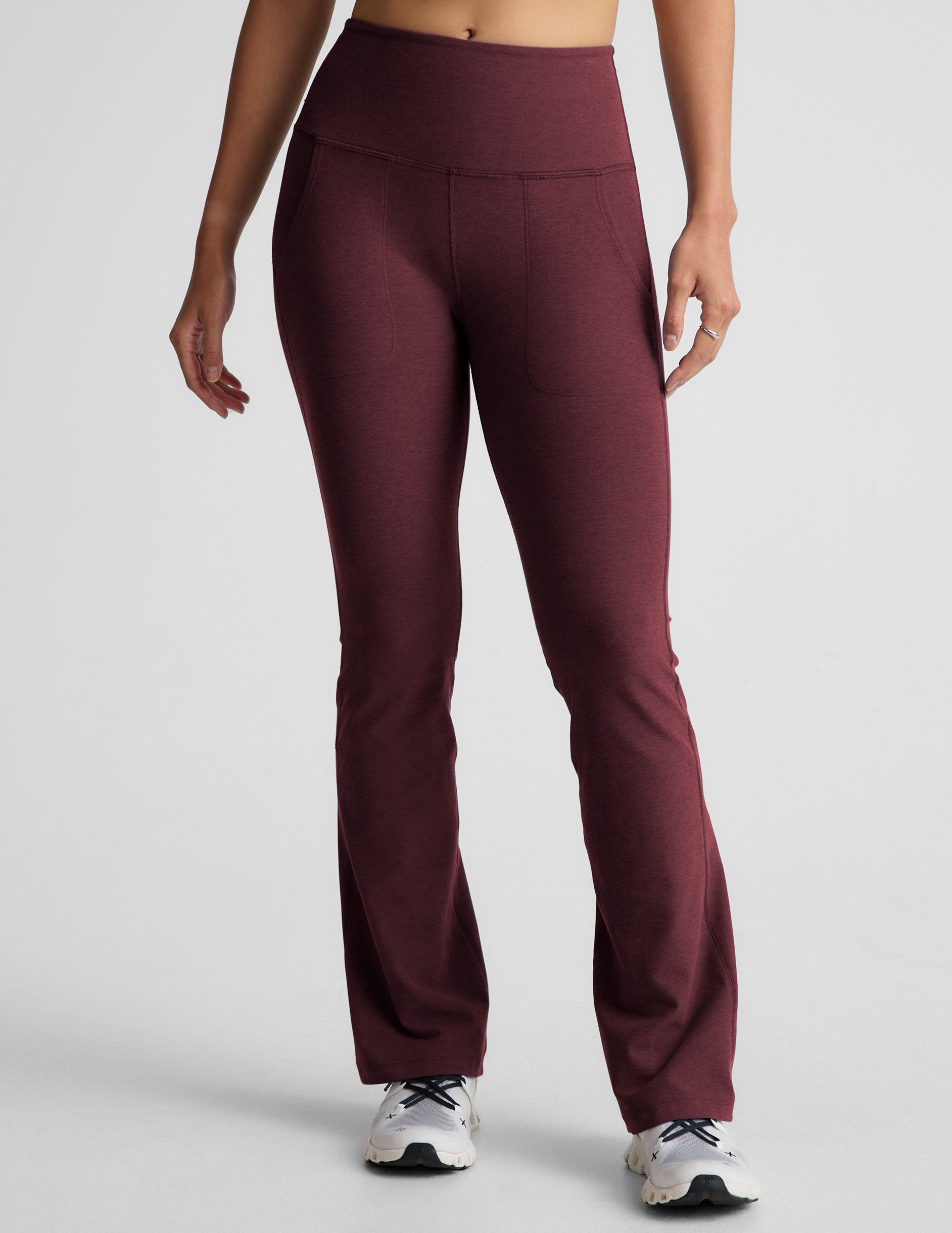 model wearing maroon bootcut pants with pockets on a light gray background.