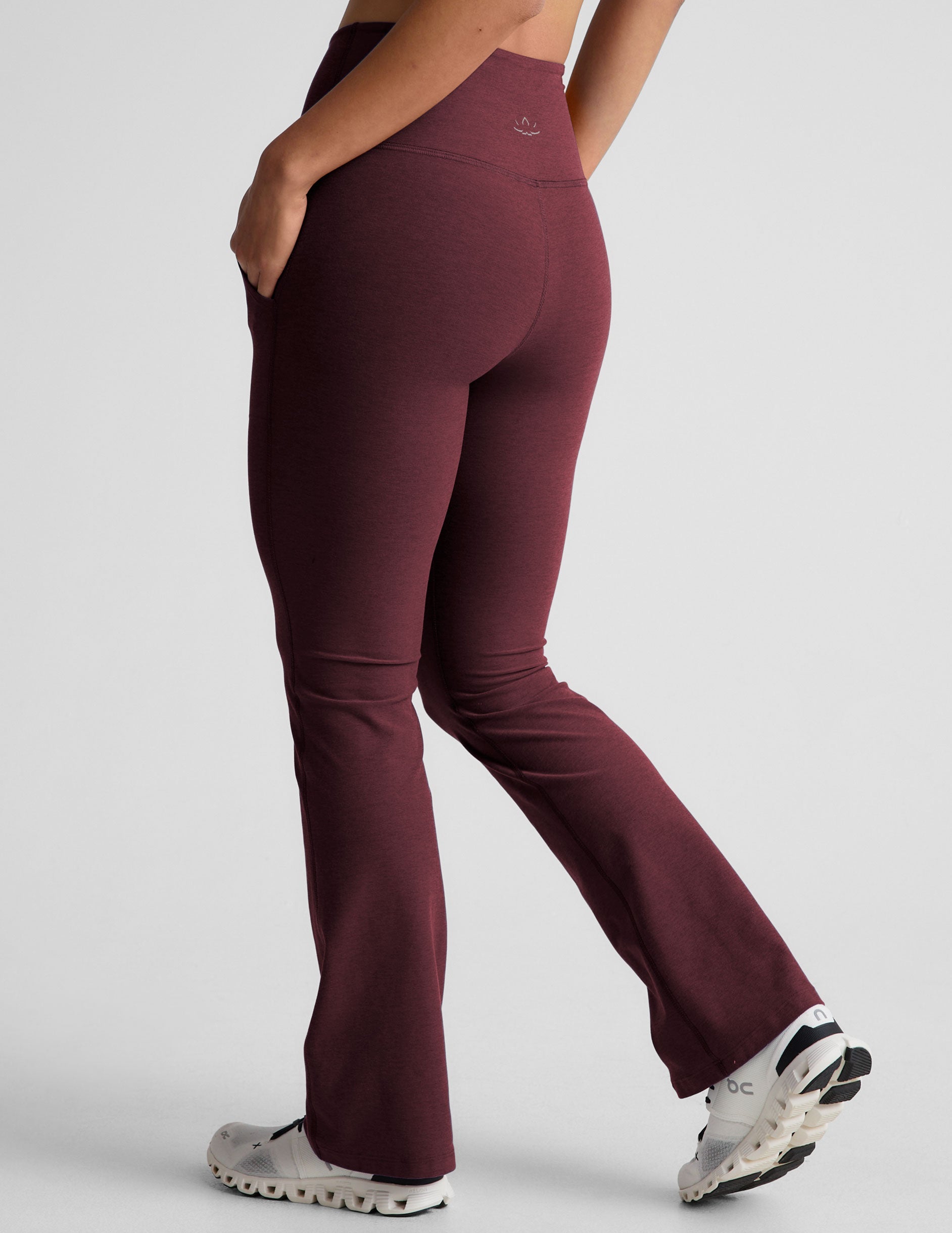 model wearing maroon bootcut pants with pockets on a light gray background.