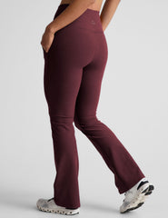 model wearing maroon bootcut pants with pockets on a light gray background.