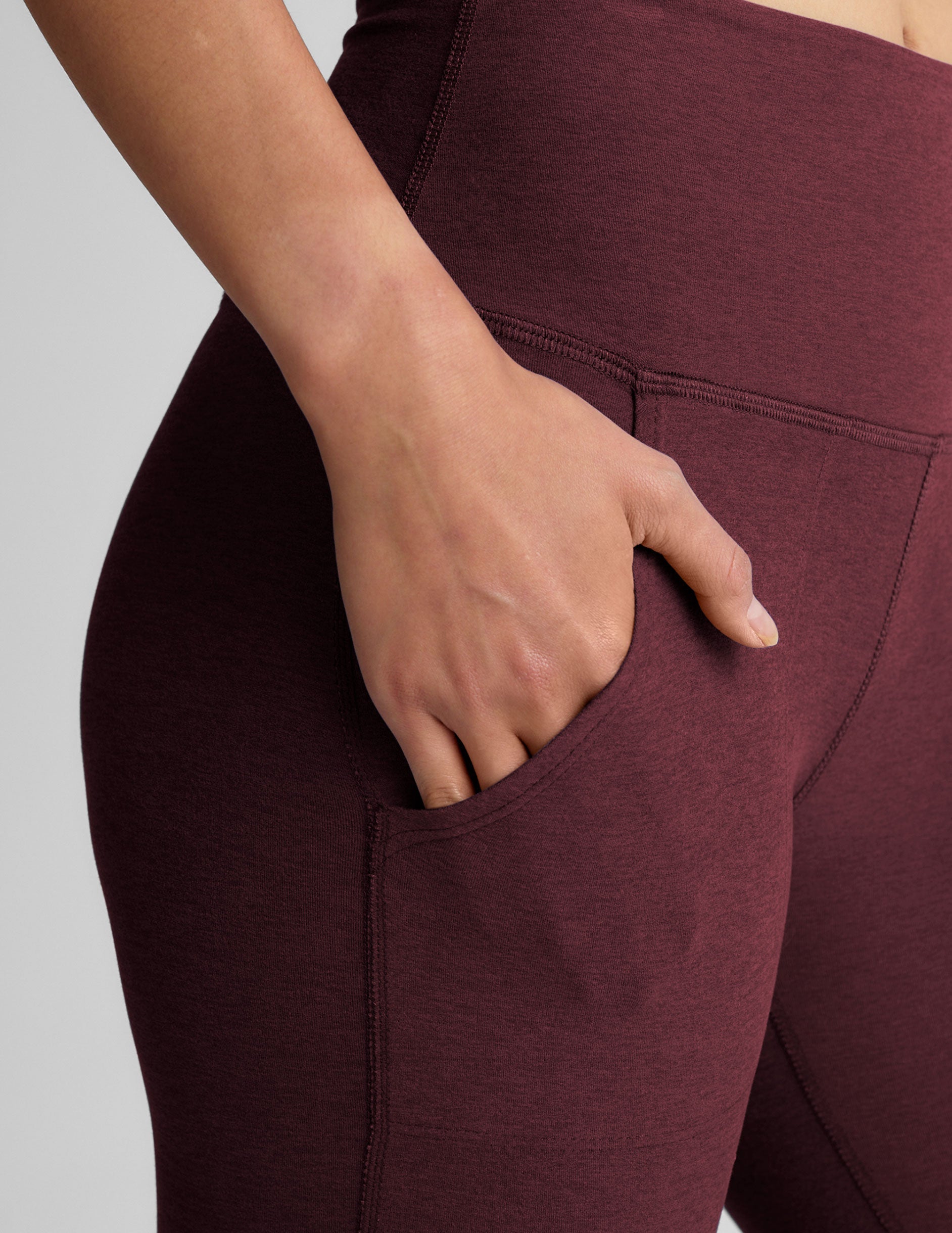 model wearing maroon bootcut pants with pockets on a light gray background.