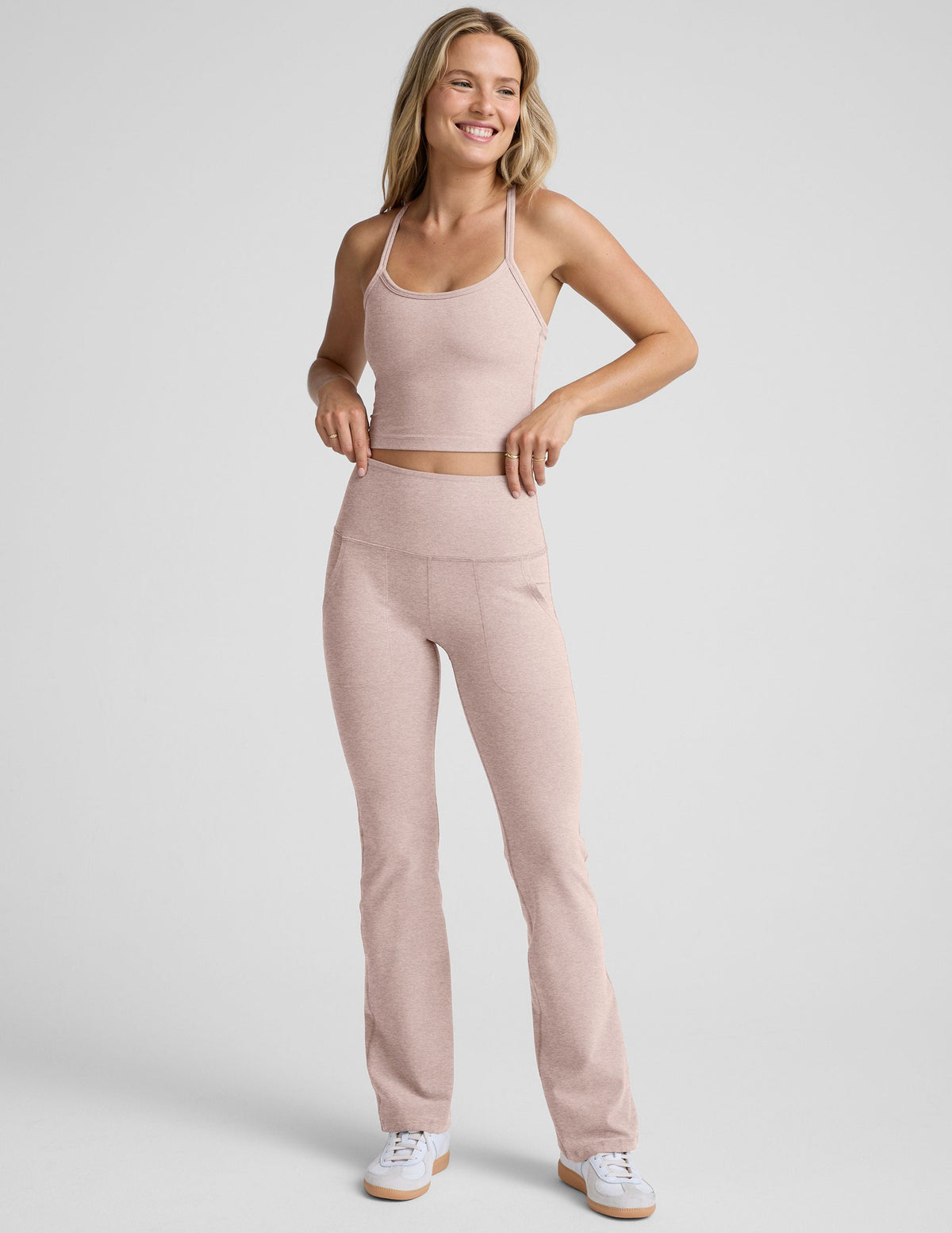 model wearing a pink cropped racerback tank top and pink high-waisted bootcut pants with pockets set on a plain background.