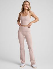 model wearing a pink cropped racerback tank top and pink high-waisted bootcut pants with pockets set on a plain background.