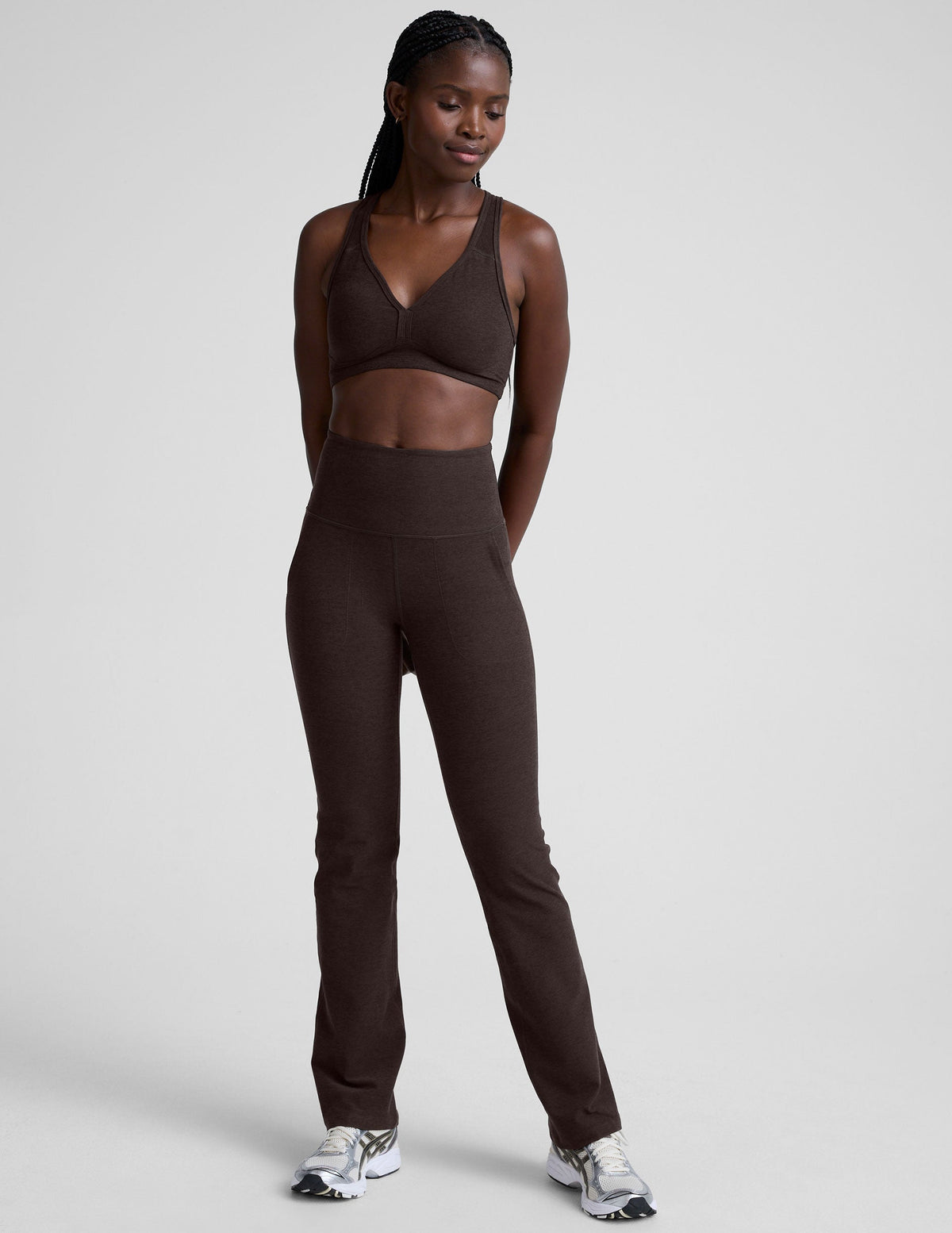 woman wearing a brown sports bra and mid-rise pants on a white background.