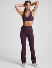model wearing a purple athletic bra and purple high-waisted bootcut pants with pockets on a plain background.