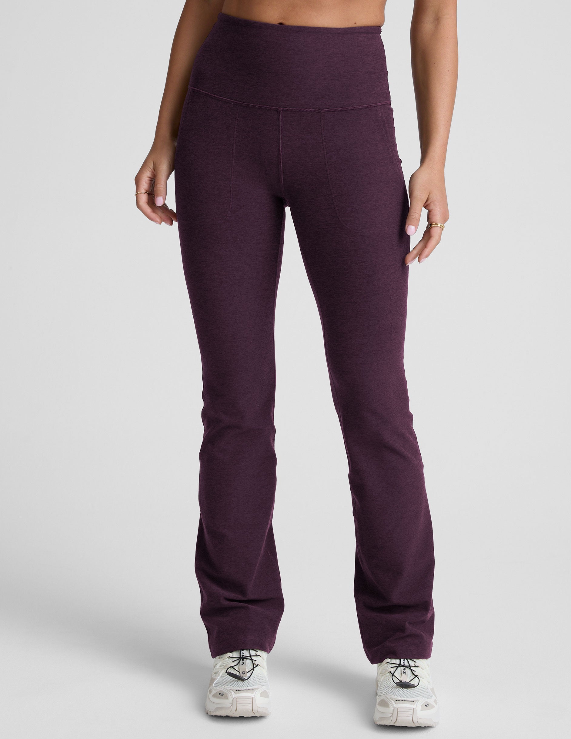 model wearing purple high-waisted bootcut pants with pockets on a plain background.