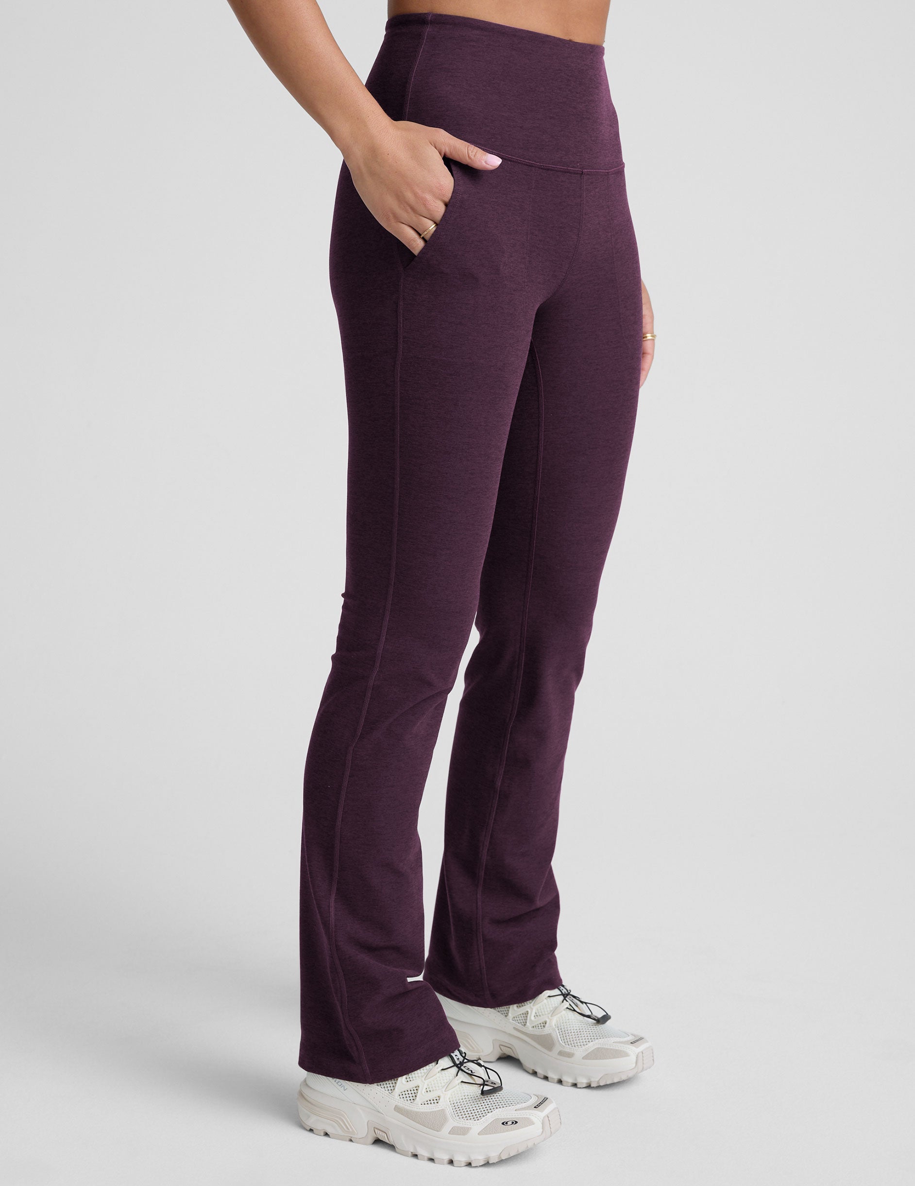 model wearing purple high-waisted bootcut pants with pockets on a plain background.