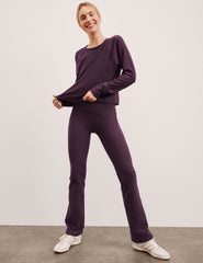 woman wearing a purple long sleeve and pants with white shoes on a plain background.