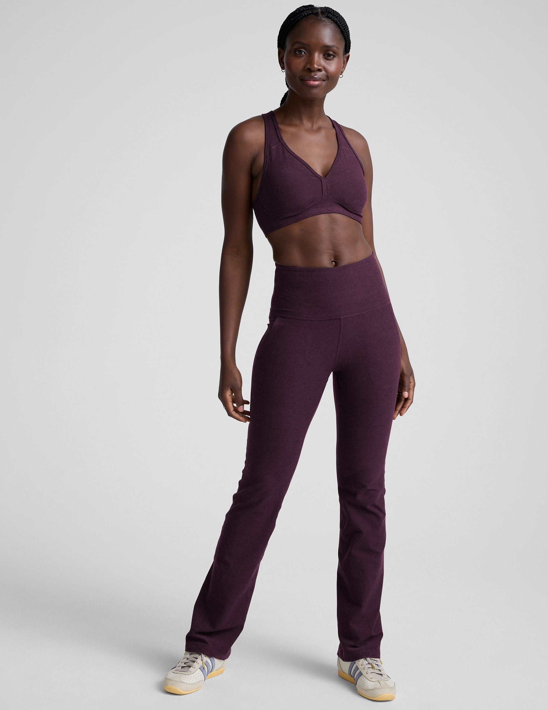 model wearing a purple athletic bra and purple high-waisted bootcut pants with pockets on a plain background.