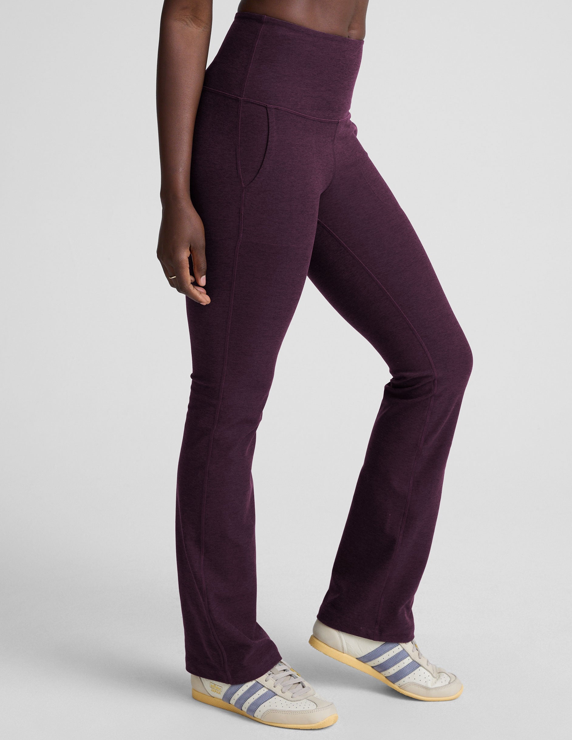 model wearing purple high-waisted bootcut pants with pockets on a plain background.