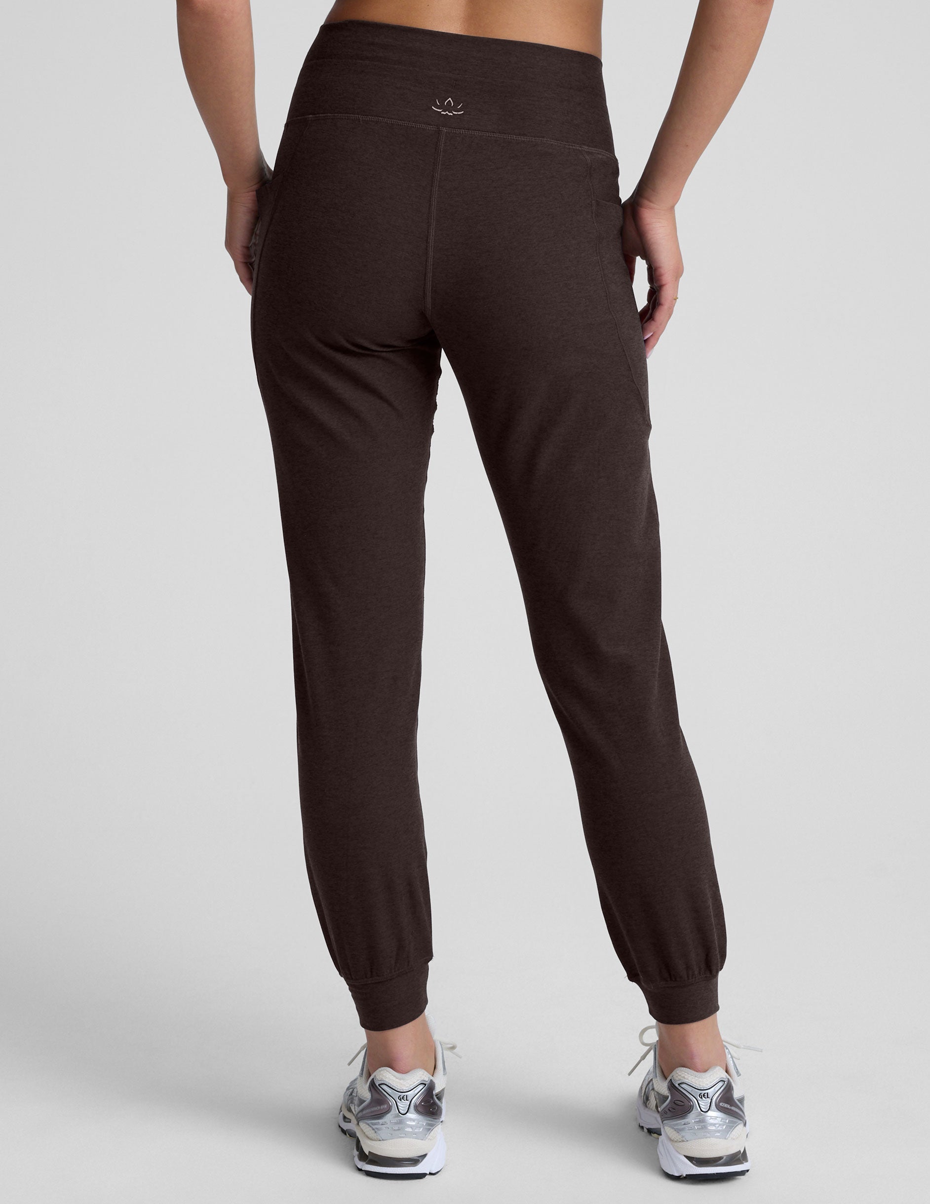 woman wearing a brown joggers with pockets on a light gray background.