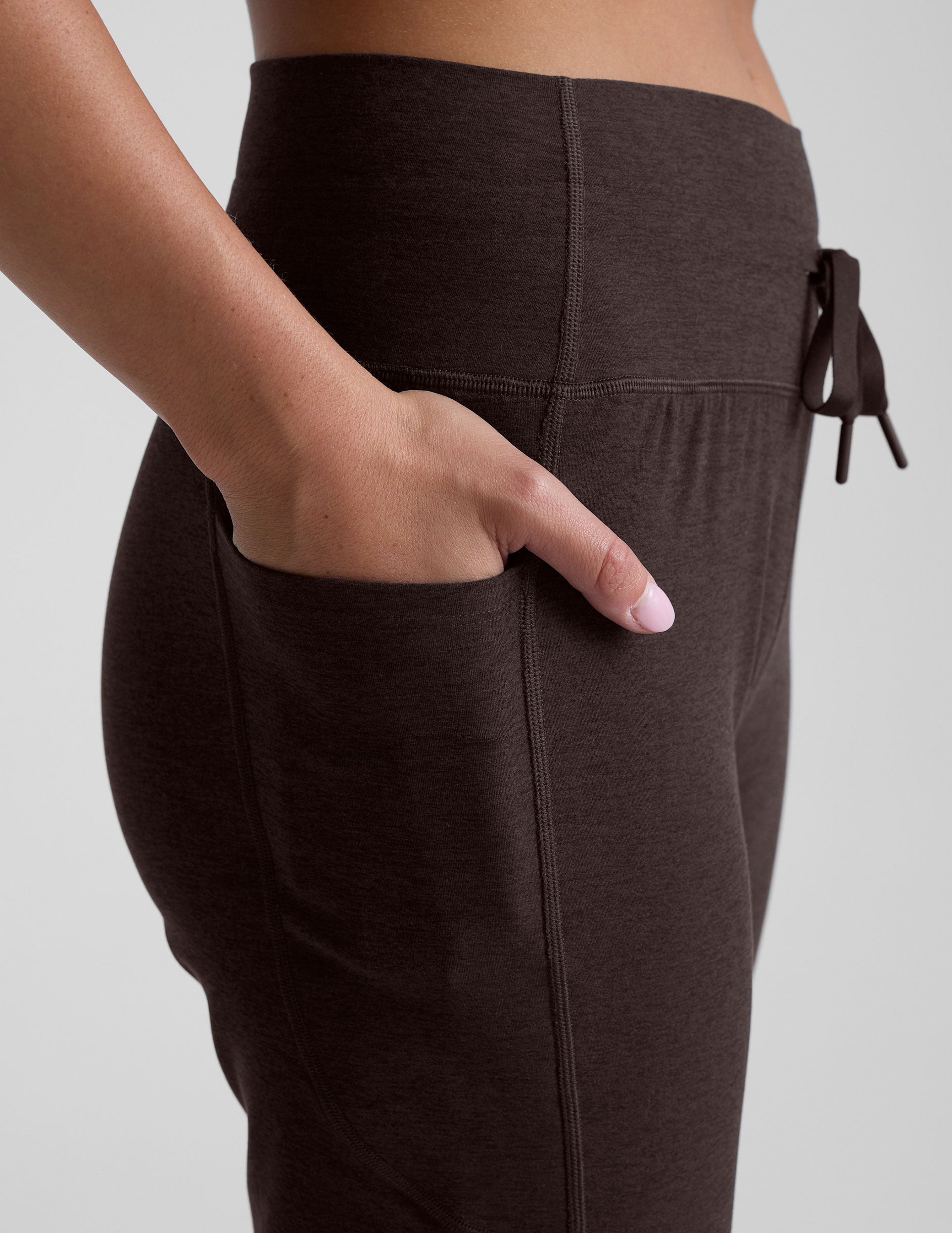 brown pants with a hand in one of the pockets on a light gray background.