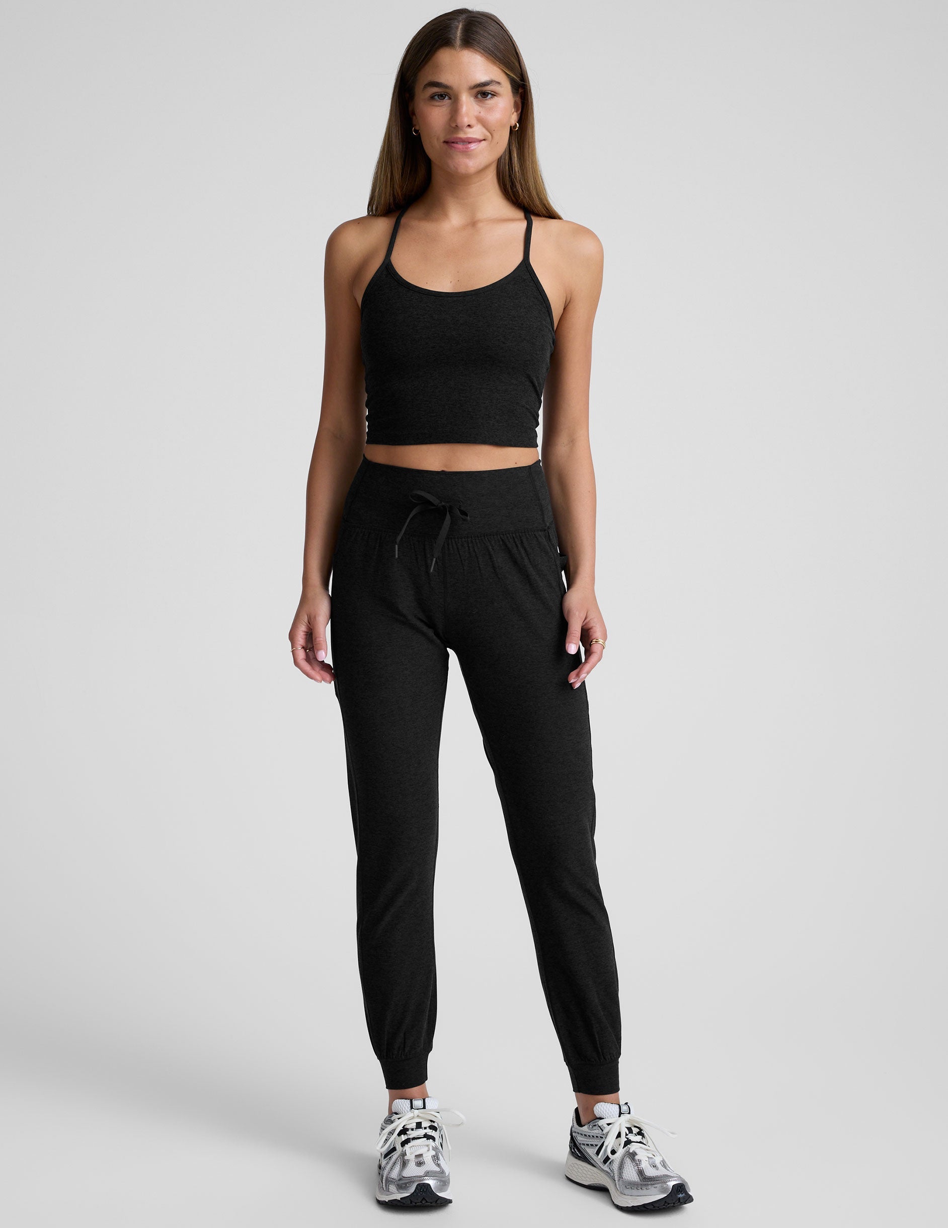 model wearing a black cropped tank and black high-waisted midi length joggers with a drawcord at waistband and pockets against a plain background.