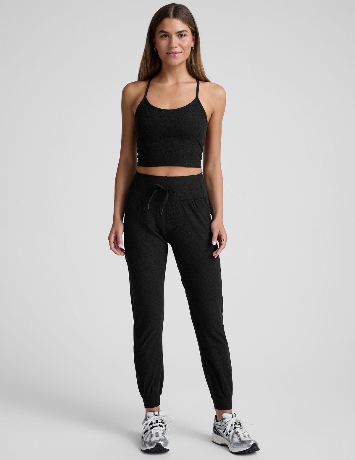 model wearing a black cropped tank and black high-waisted midi length joggers with a drawcord at waistband and pockets against a plain background.
