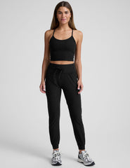 model wearing a black cropped tank and black high-waisted midi length joggers with a drawcord at waistband and pockets against a plain background.