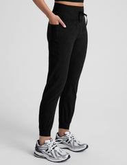 model wearing black high-waisted midi length joggers with a drawcord at waistband and pockets against a plain background.