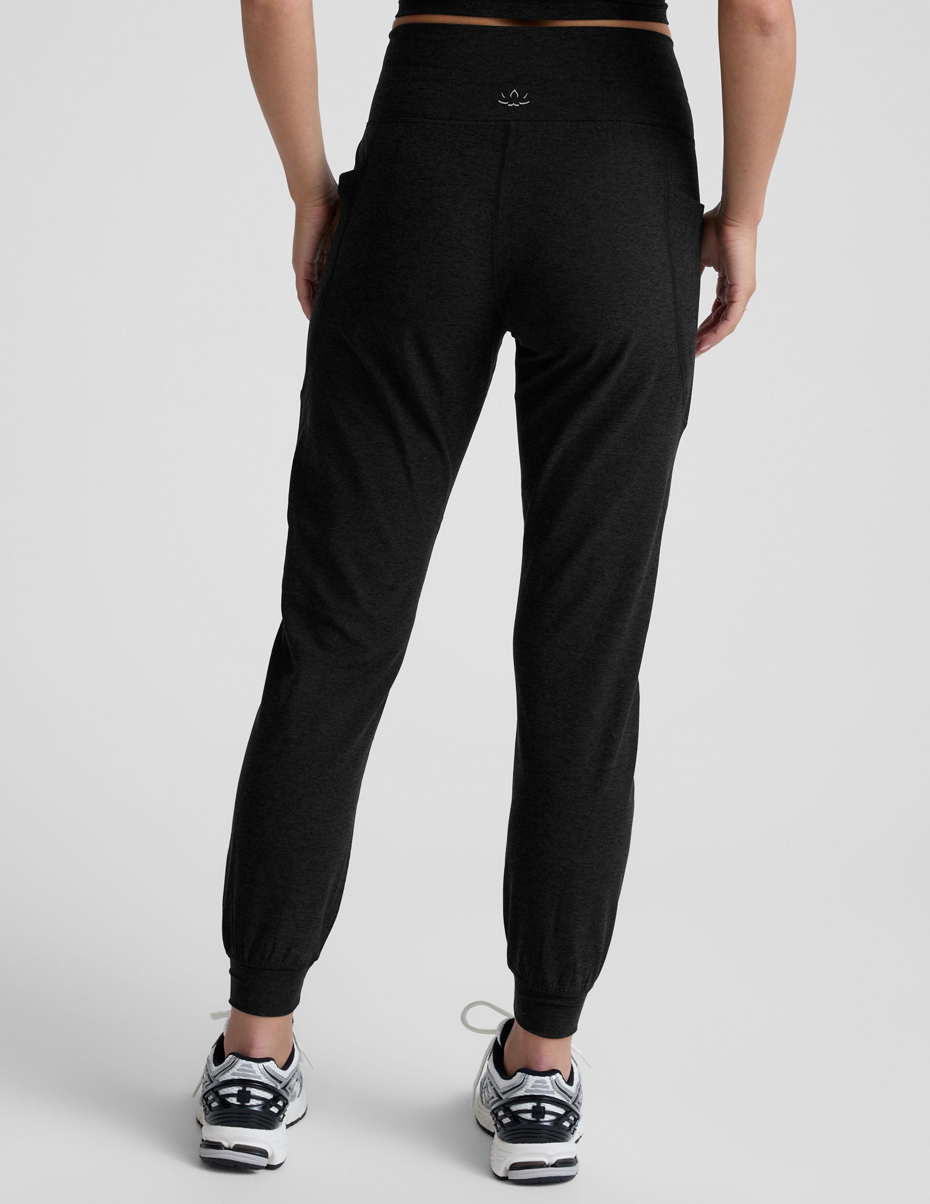 model wearing black high-waisted midi length joggers with a drawcord at waistband and pockets against a plain background.