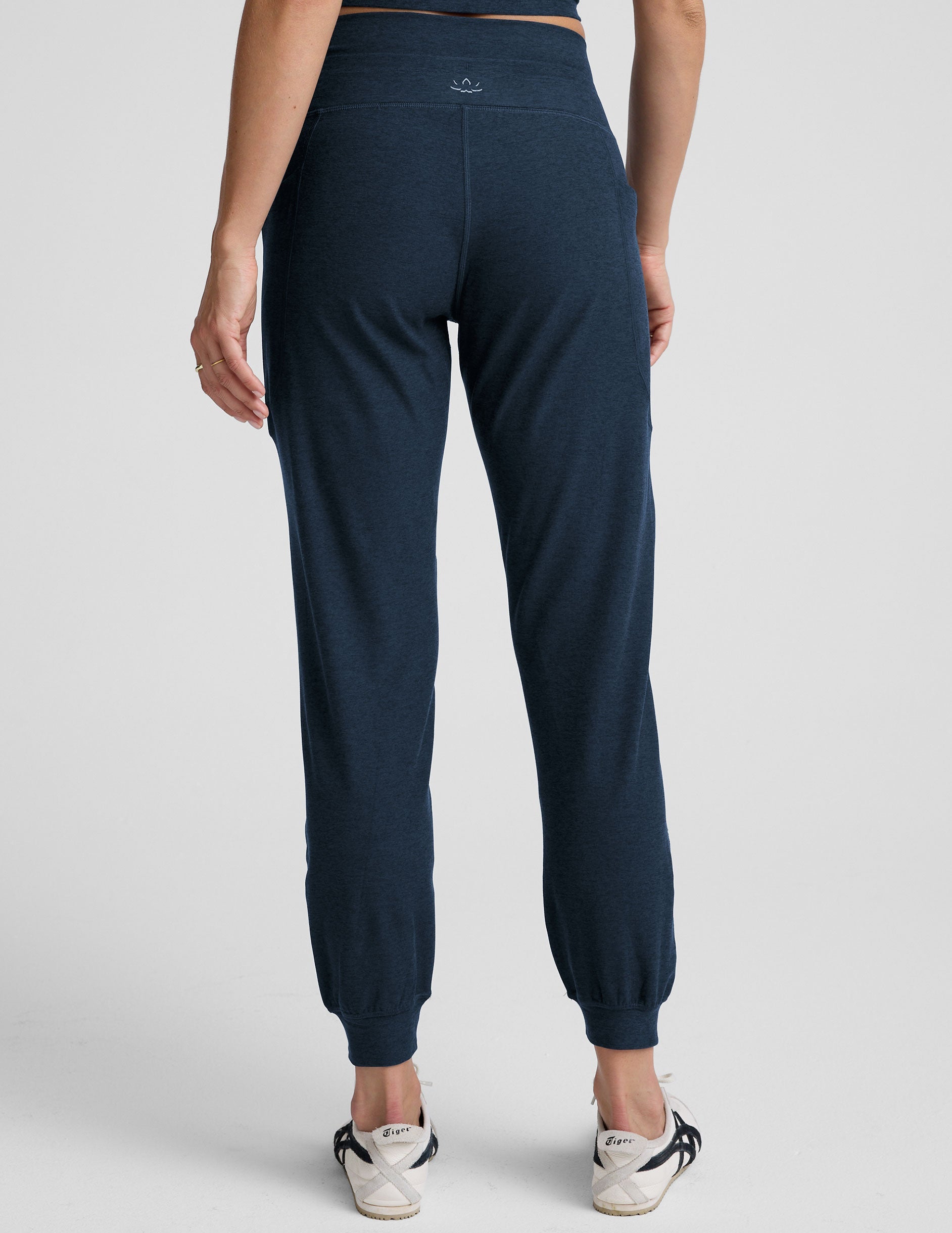 model wearing navy blue high-waisted midi length joggers with a drawcord at waistband and pockets athletic outfit on a plain background.