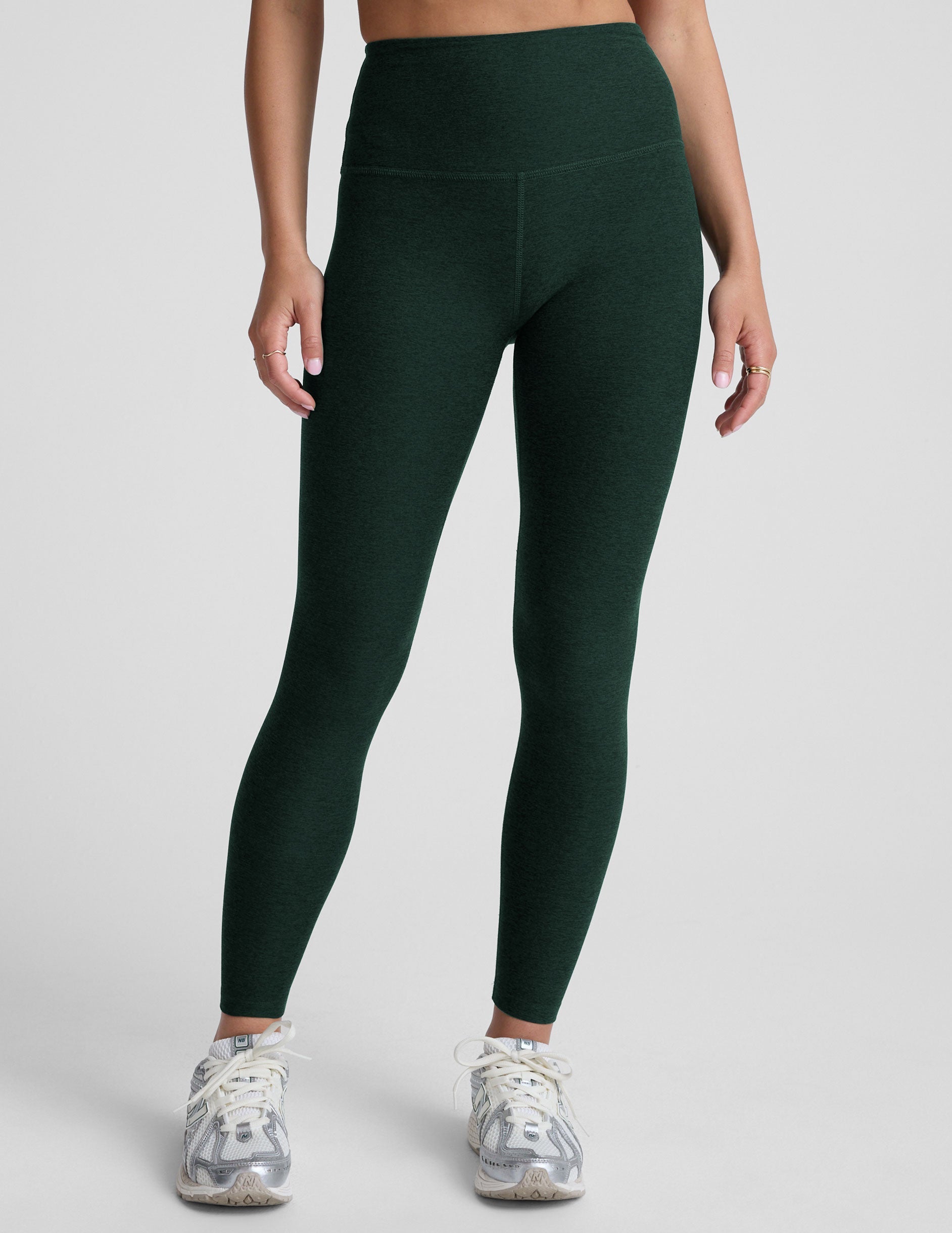 model wearing green high-waisted full length leggings on a plain background.