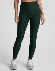 model wearing green high-waisted full length leggings on a plain background.