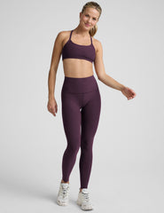 model wearing a purple racerback bra and purple high-waisted full length leggings on a plain background.