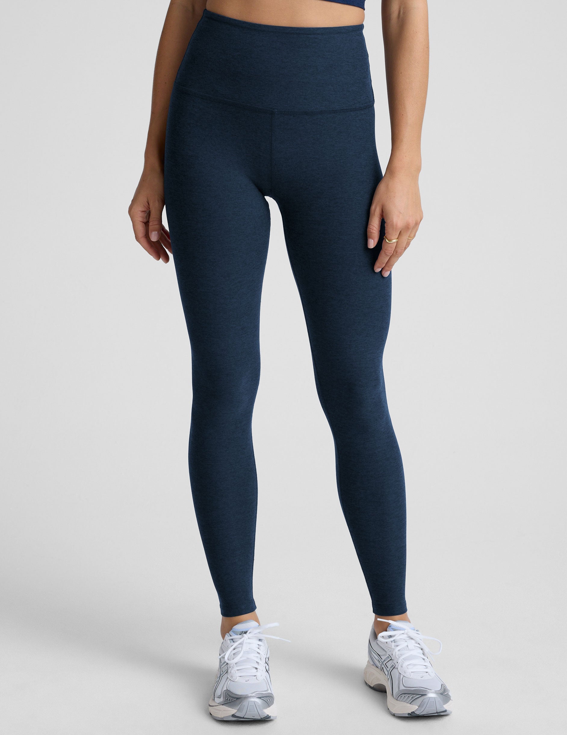 woman is wearing blue high-waisted midi length leggings against a plain background.