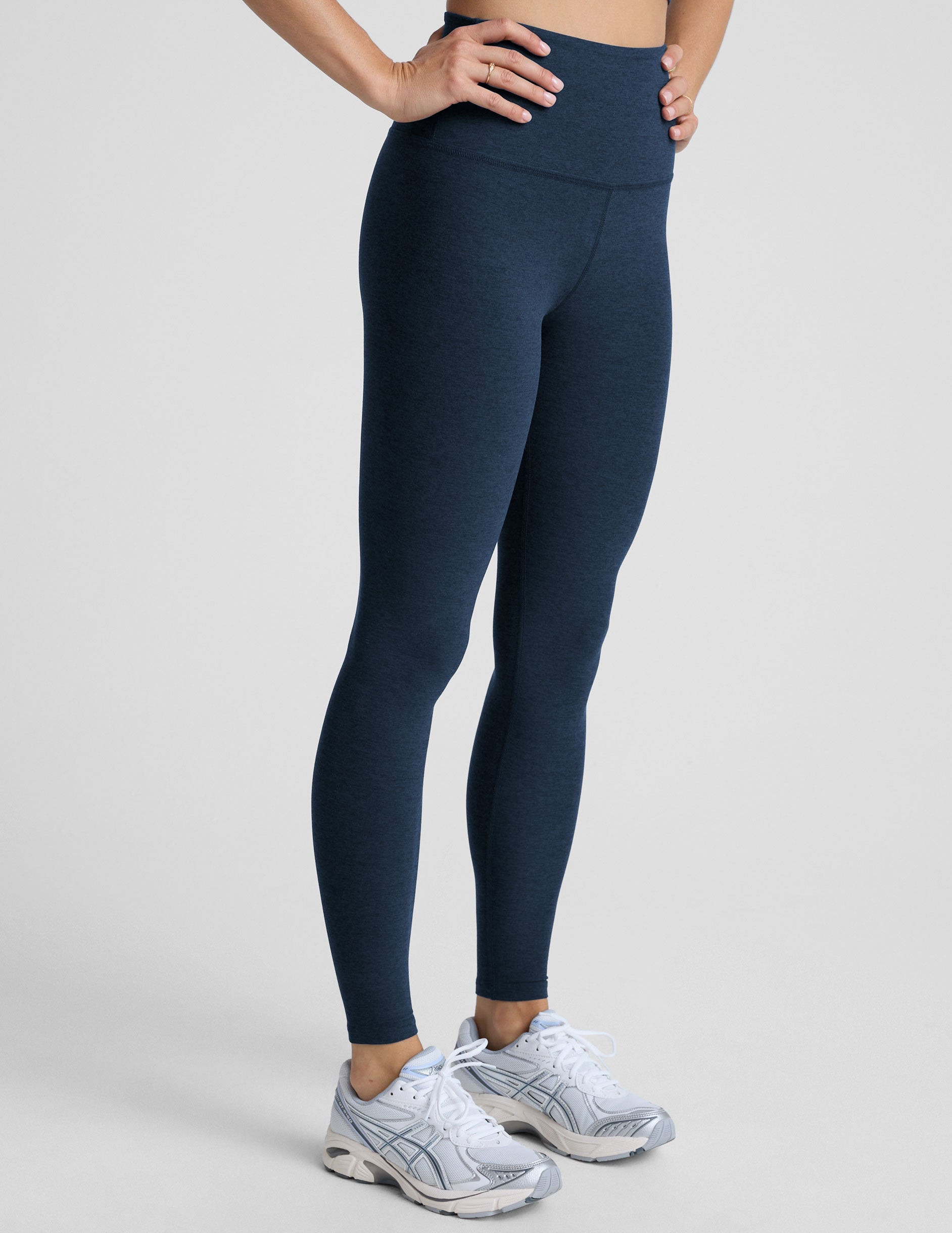 woman is wearing blue high-waisted midi length leggings against a plain background.