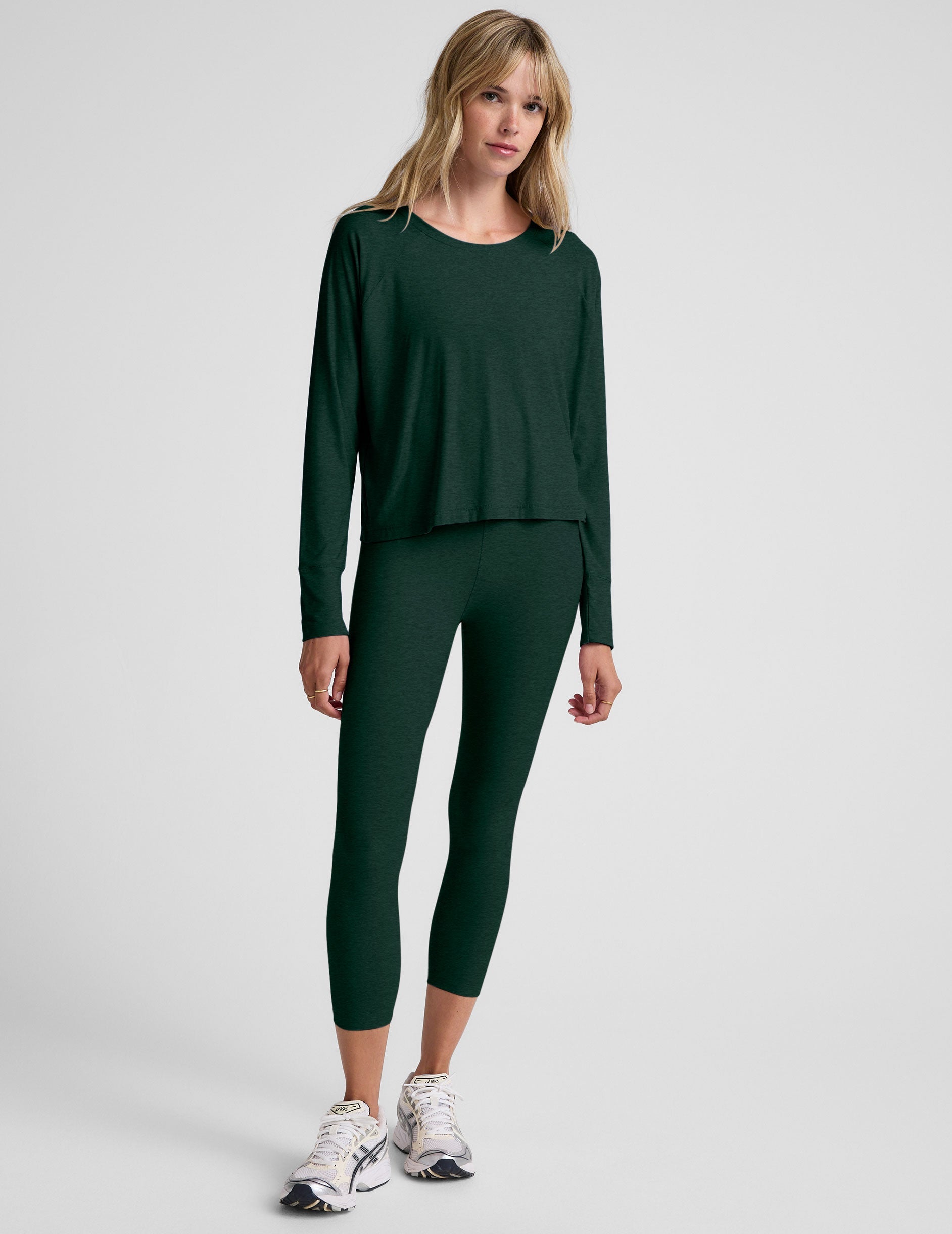 model wearing a green long sleeve and green high-waisted capri leggings on a plain background.
