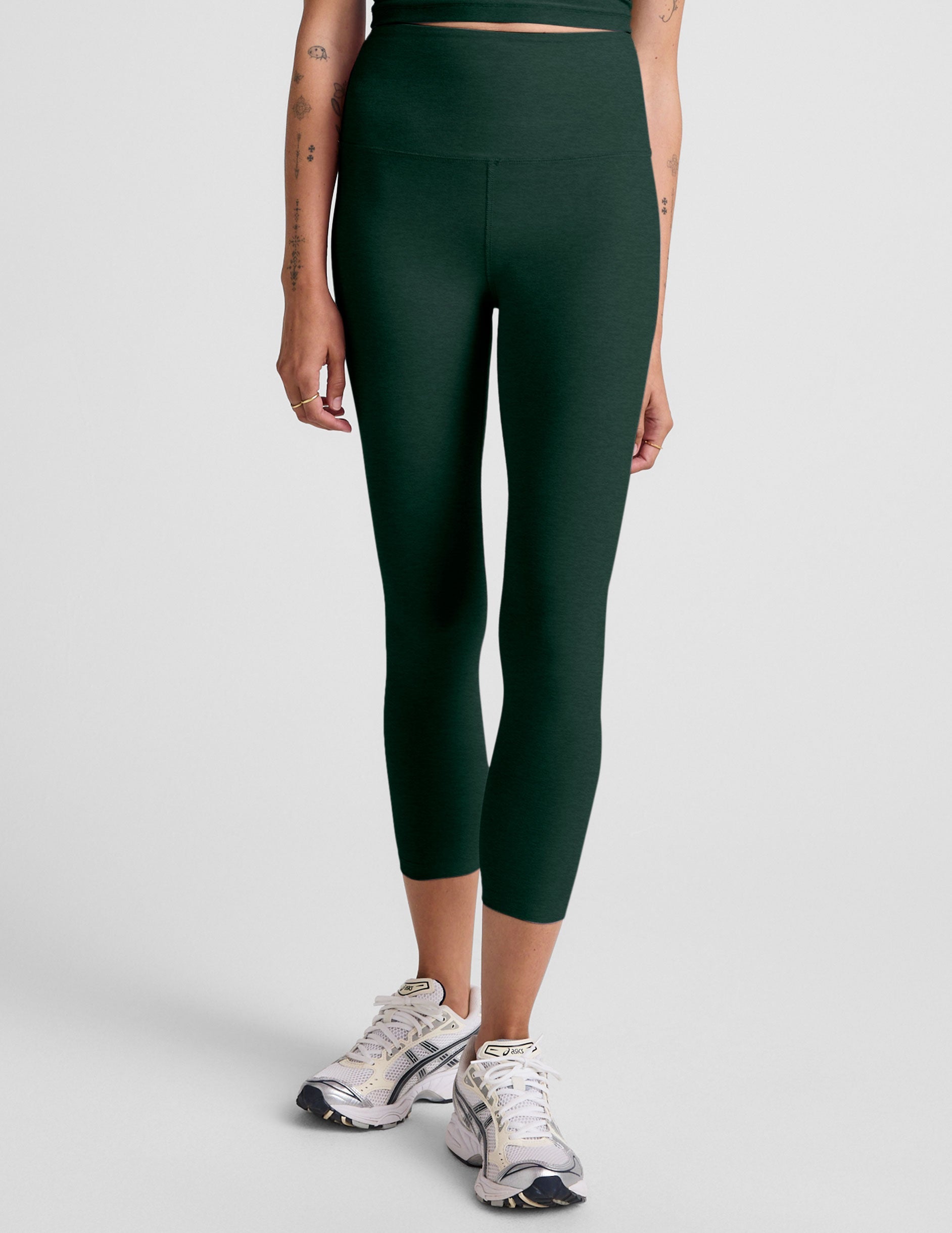 model wearing green high-waisted capri leggings on a plain background.