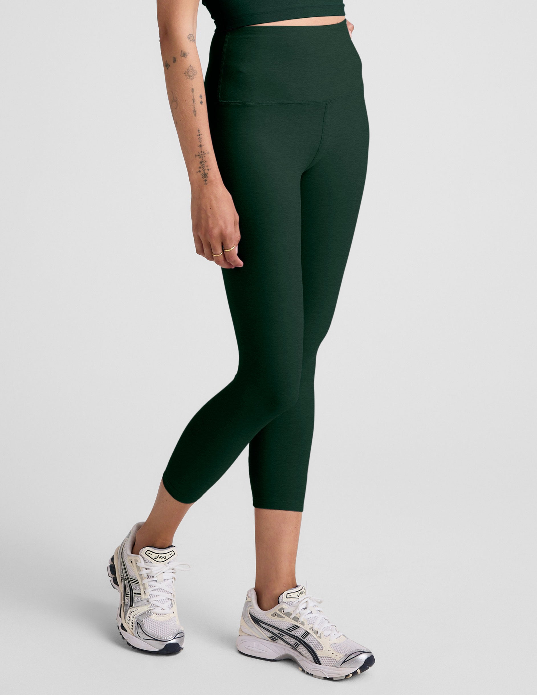 model wearing green high-waisted capri leggings on a plain background.