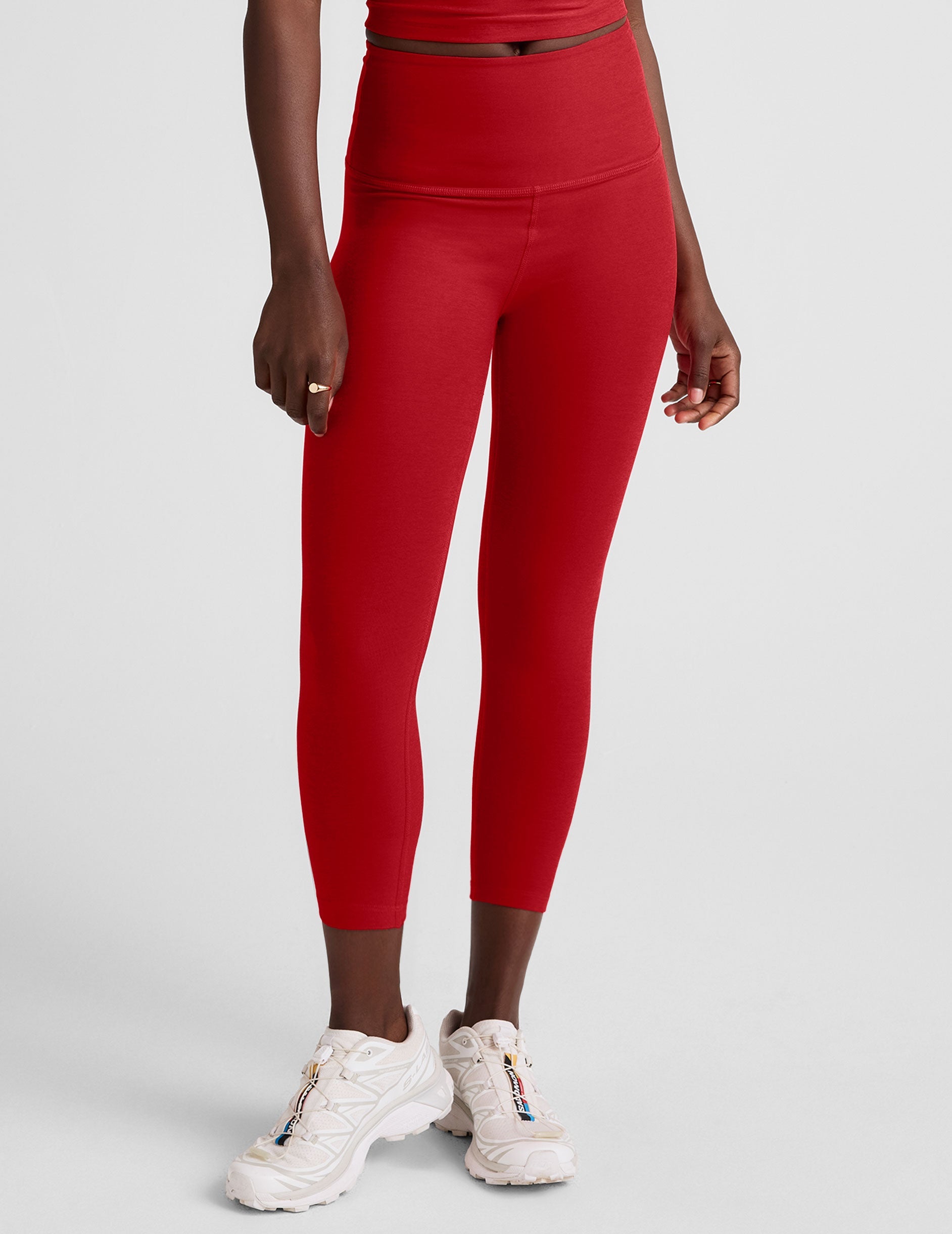 woman wearing a red cropped tank and capri length leggings on a plain background.