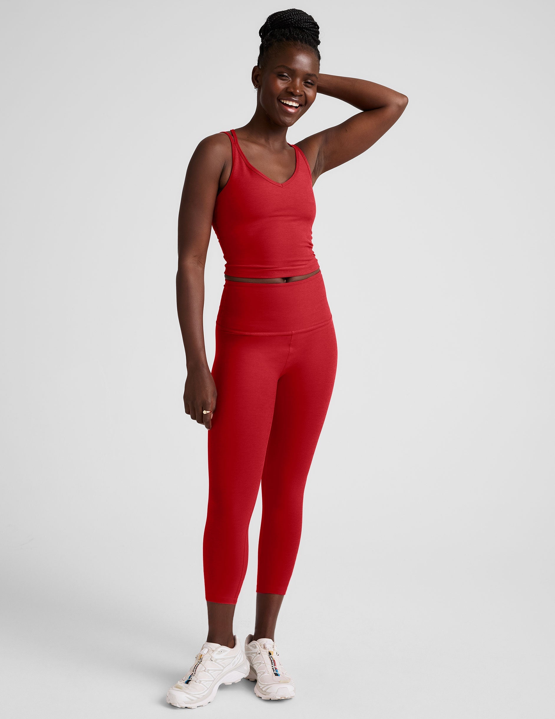 woman wearing a red cropped tank and capri length leggings on a plain background.