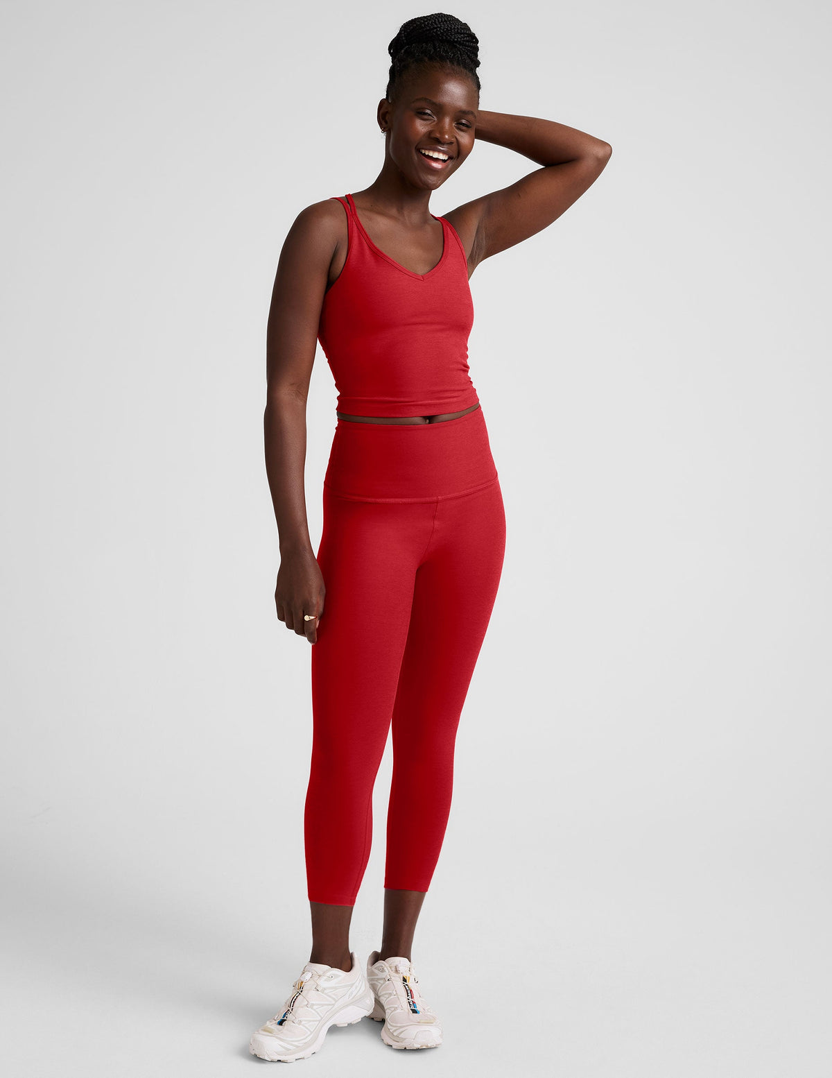 woman wearing a red cropped tank and capri length leggings on a plain background.