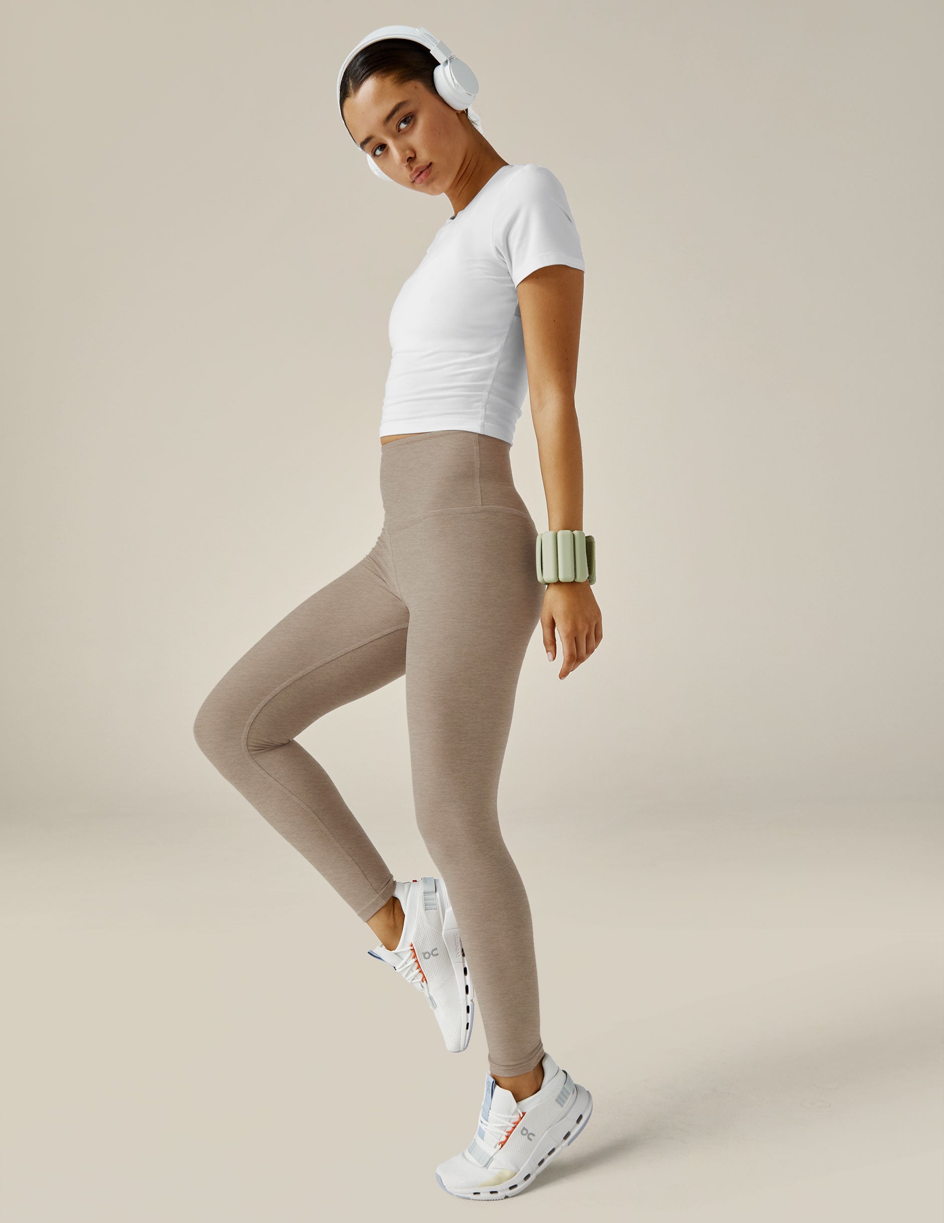 woman wearing beige leggings and a white top on a beige background.