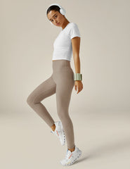 woman wearing beige leggings and a white top on a beige background.