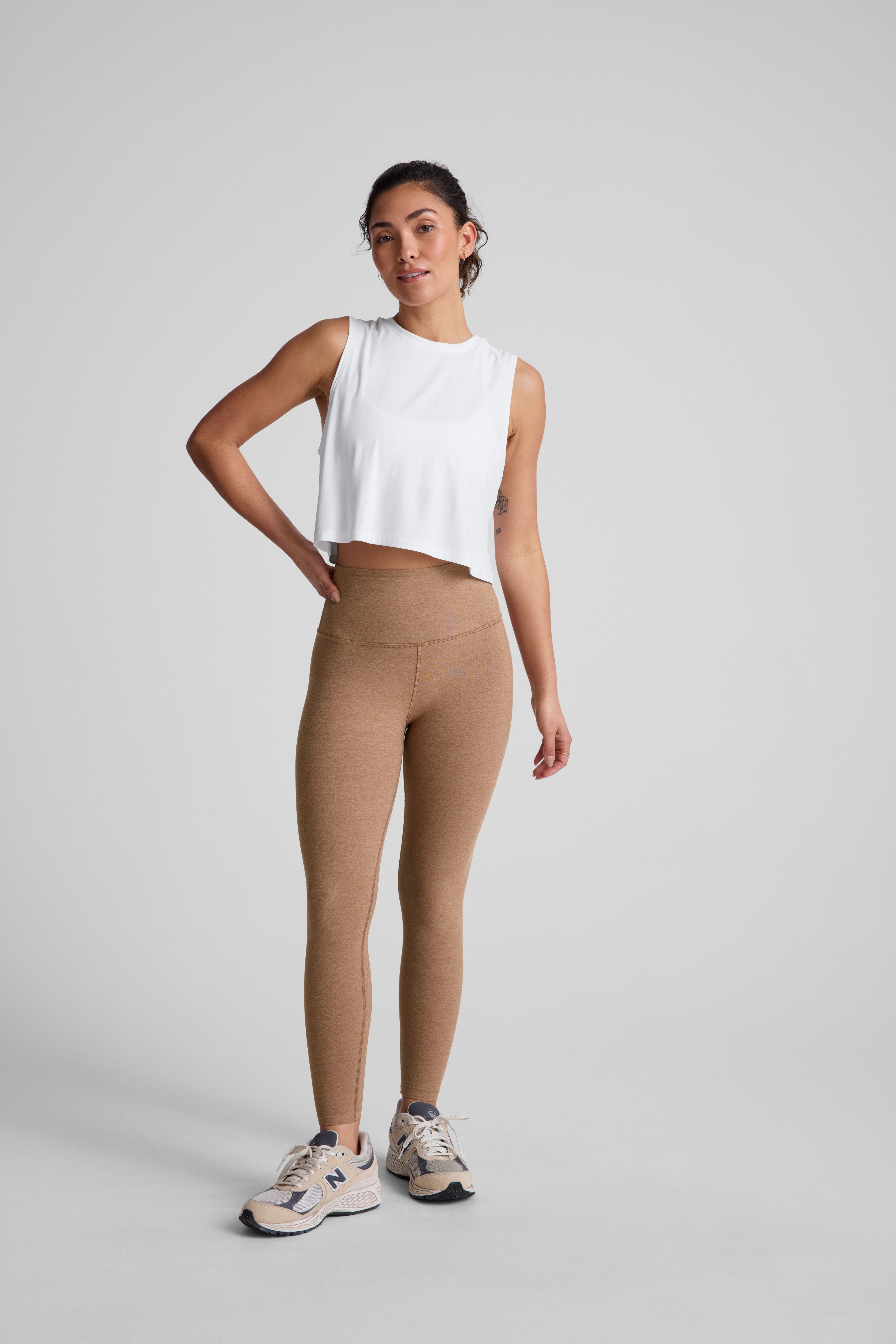 model is wearing brown high-waisted midi leggings and a white tank top.