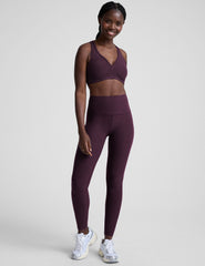 model wearing a purple sports bra and purple high-waisted midi length leggings  on a light background.