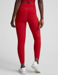 woman wearing a red slim racerback cropped tank top and high-waisted midi length leggings against a plain background.