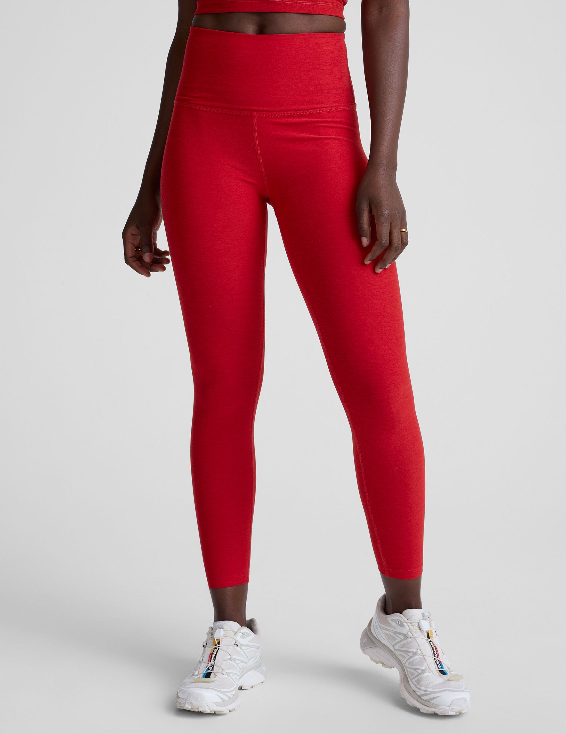 woman wearing a red slim racerback cropped tank top and high-waisted midi length leggings against a plain background.