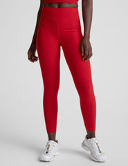 woman wearing a red slim racerback cropped tank top and high-waisted midi length leggings against a plain background.