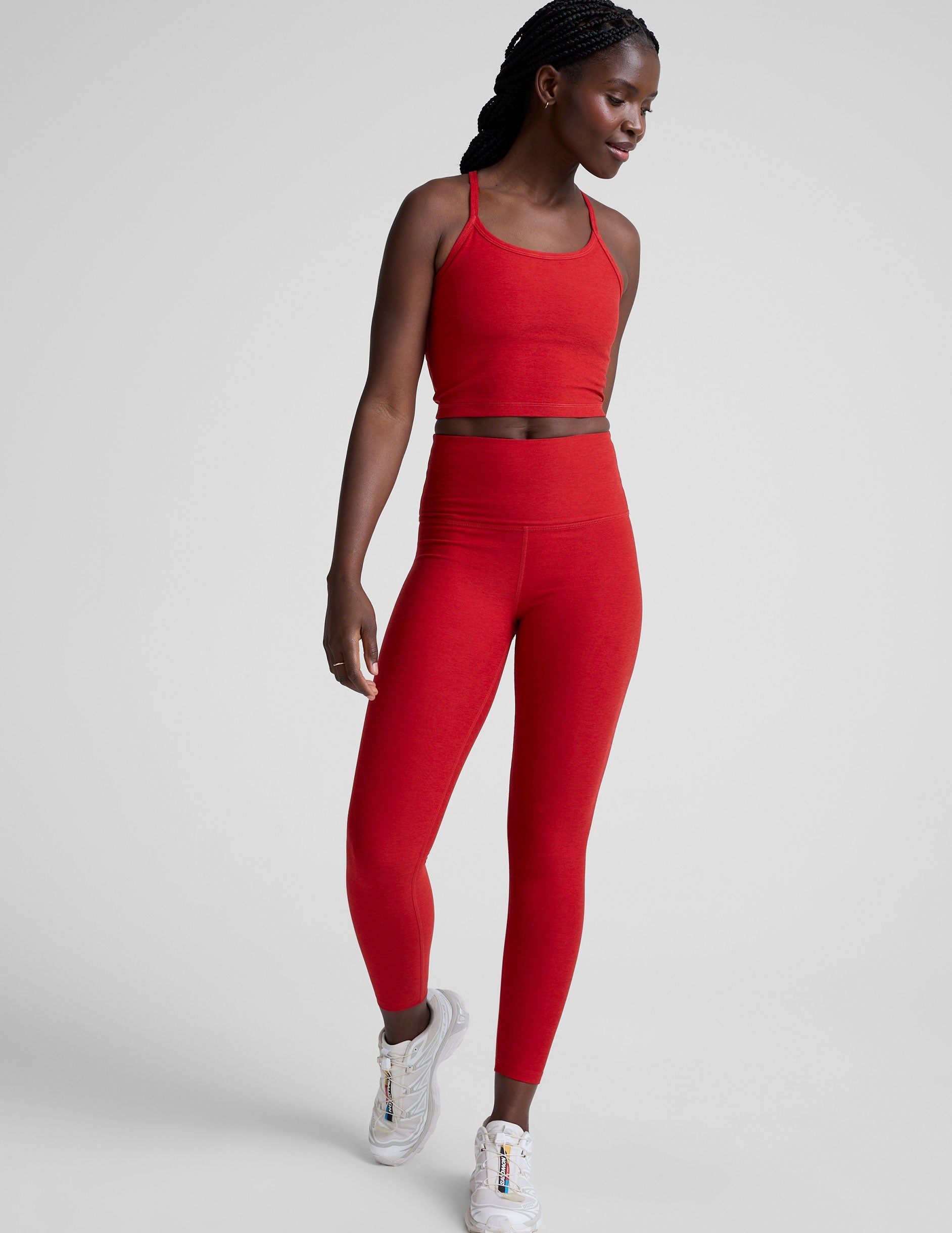 woman wearing a red slim racerback cropped tank top and high-waisted midi length leggings against a plain background.
