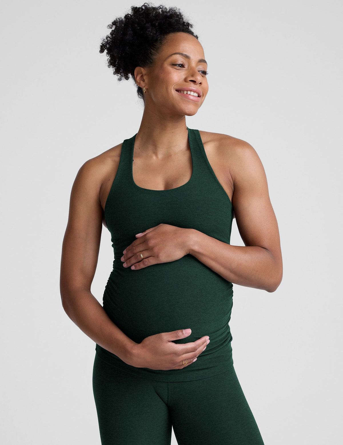 model wearing a green maternity racerback tank and green maternity midi length leggings on a plain background.