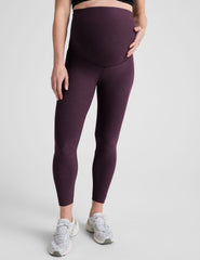 model wearing a purple maternity racerback tank and purple maternity midi length leggings on a plain background.
