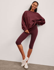 model is wearing red high-waisted pedal pusher length leggings.