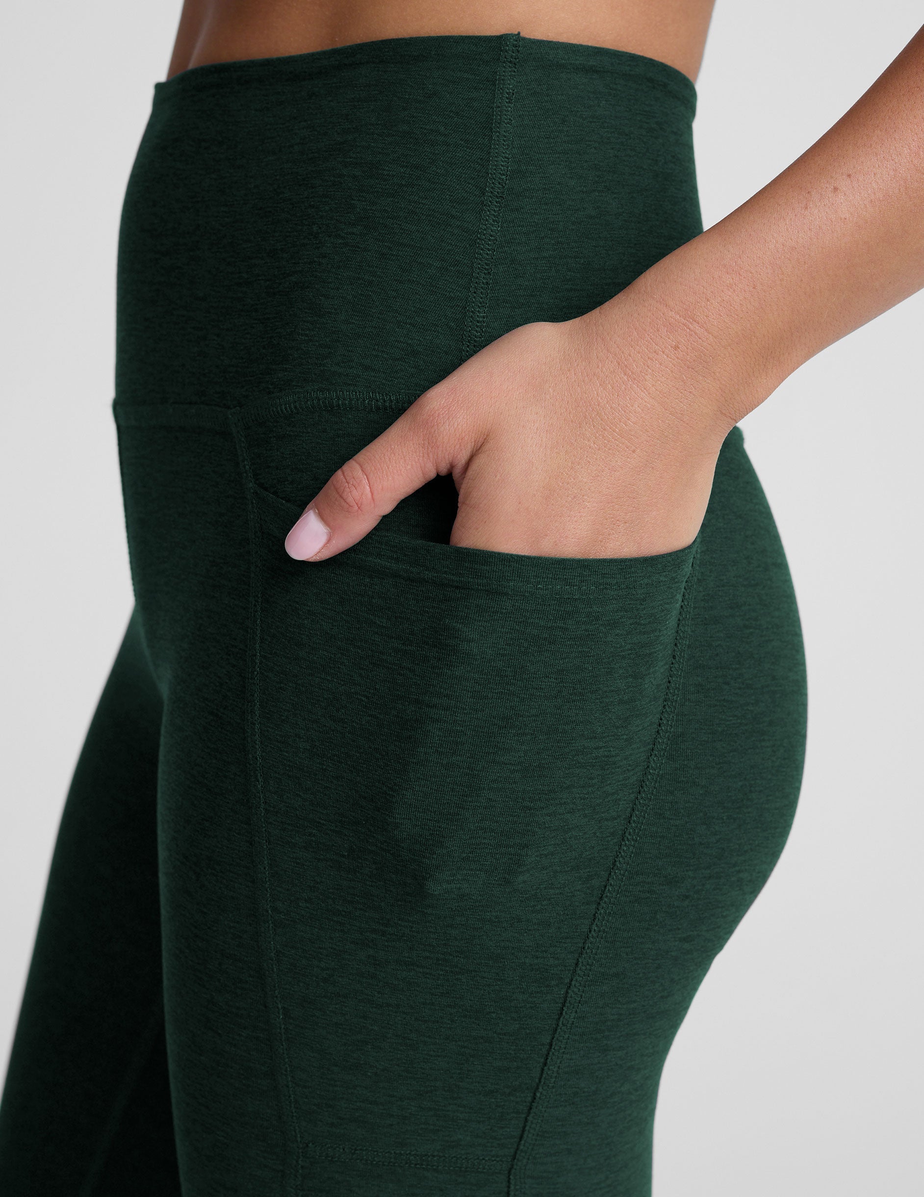 model is wearing green high-waisted midi length leggings with pockets on a plain background.