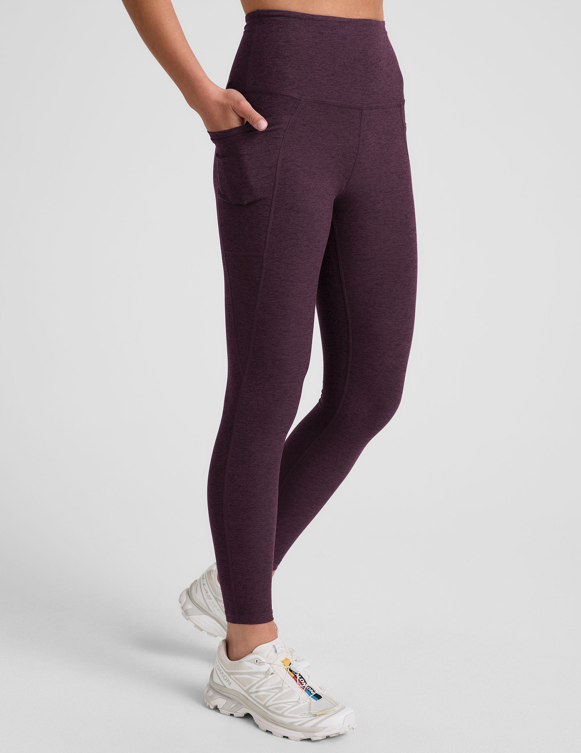model wearing a purple t-shirt and purple high-waisted midi length leggings with pockets on a light gray background.