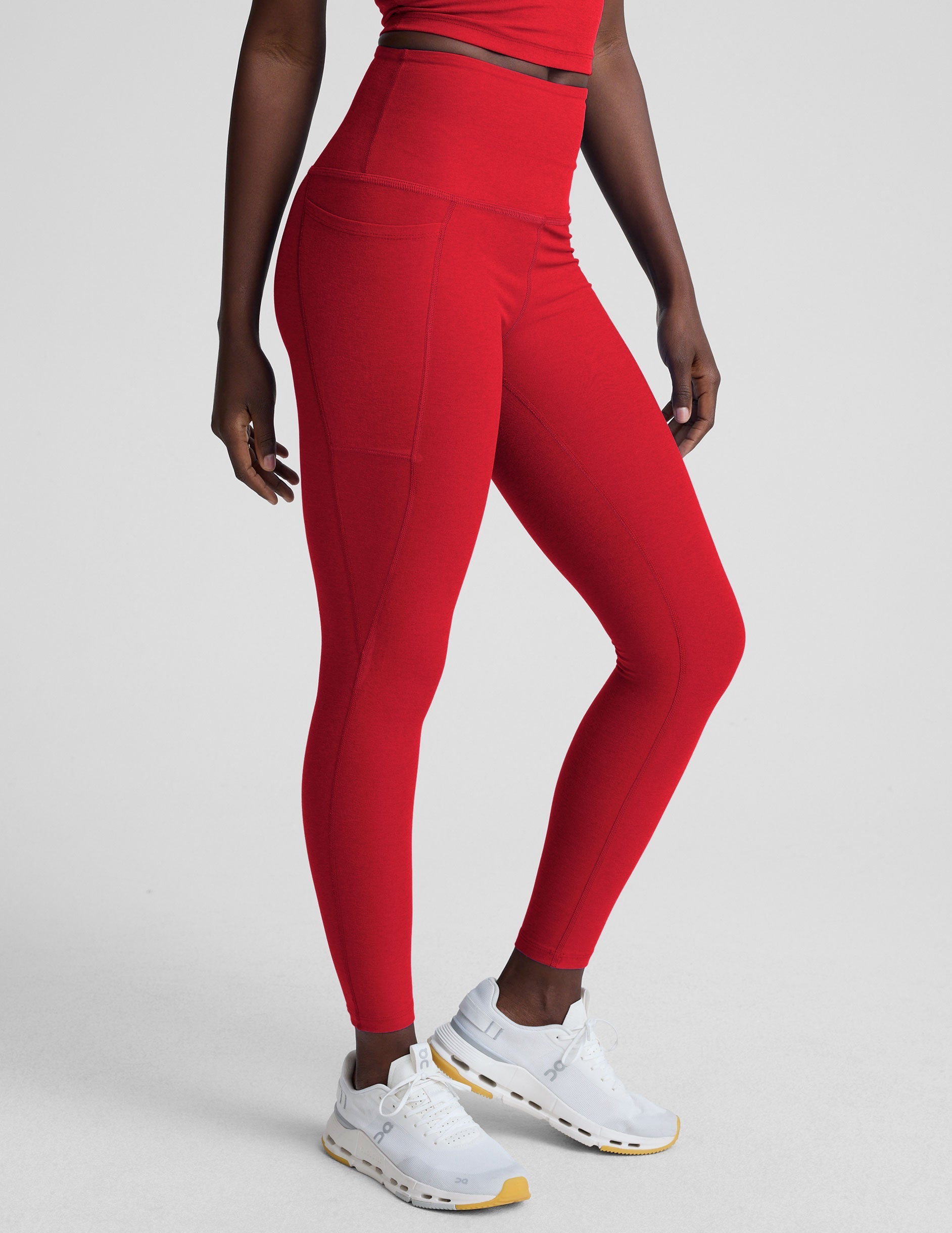 woman wearing a red high-waisted midi length pocket leggings on a plain background.