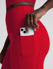 woman wearing a red high-waisted midi length pocket leggings on a plain background.
