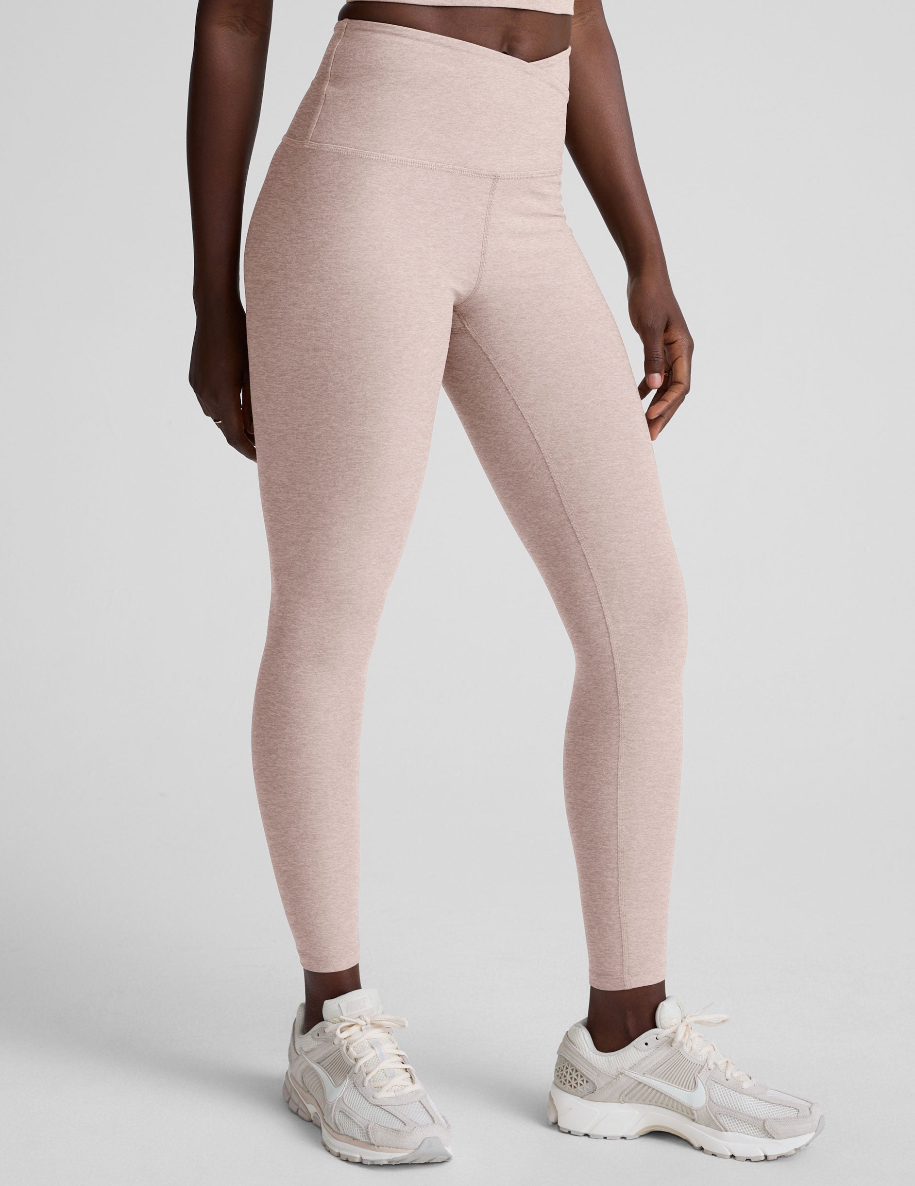 model wearing pink high-waisted leggings with a front crossover detail on a plain background.