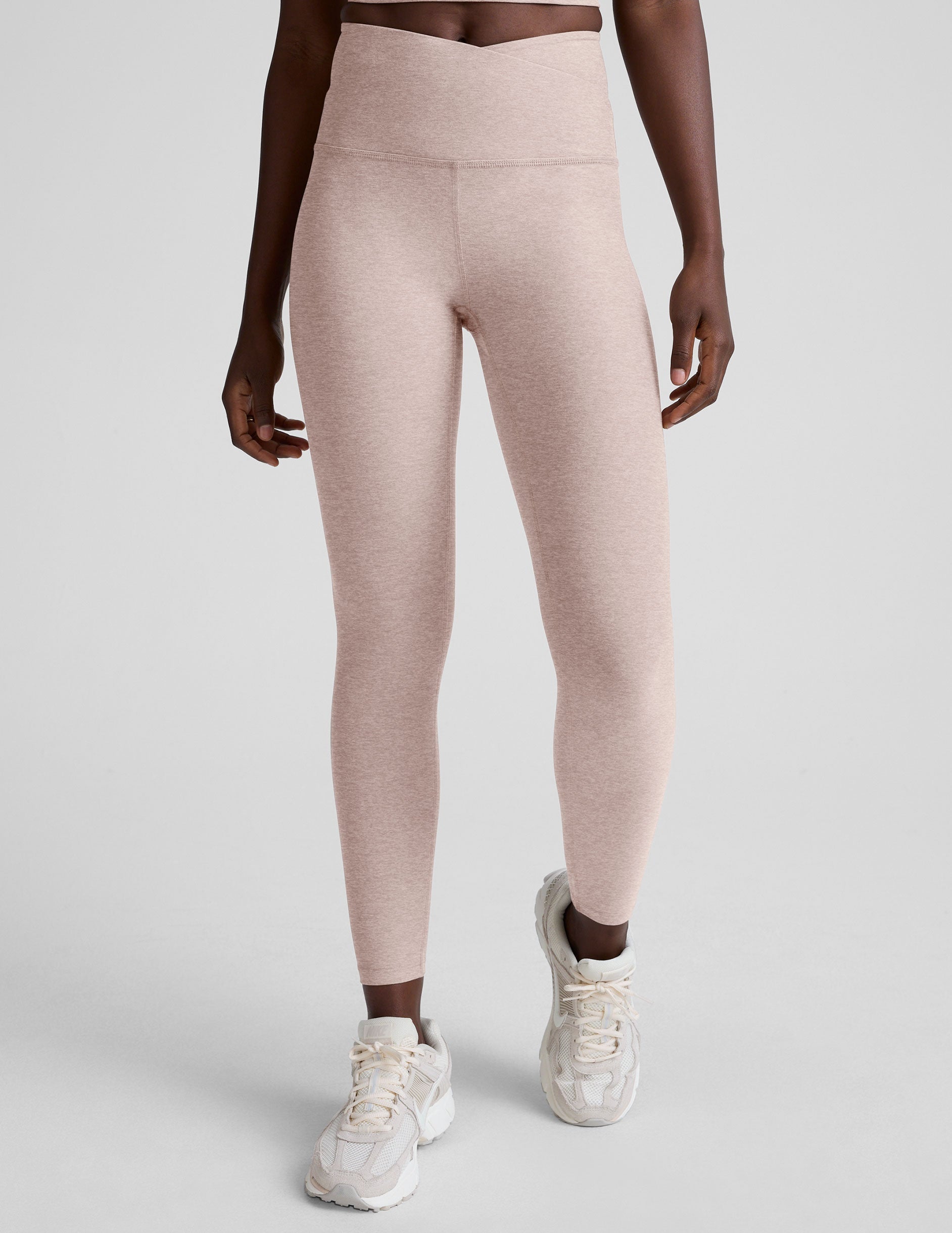 model wearing pink high-waisted leggings with a front crossover detail on a plain background.