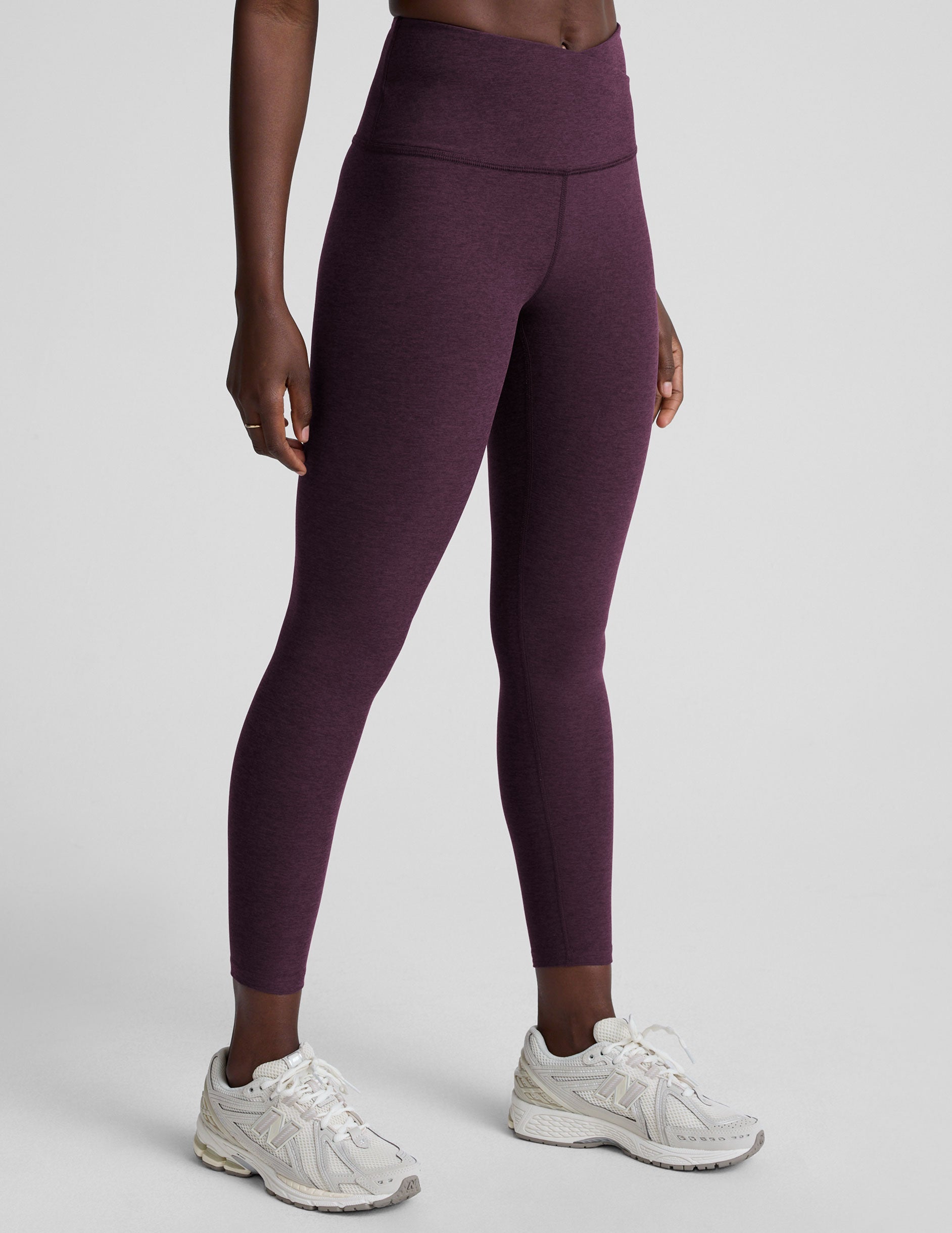 model wearing purple high-waisted midi length leggings with a front crossover detail on the waistband on a plain background.